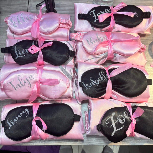 Set of personalised pink and white sleep masks with names printed on them, displayed on a table.