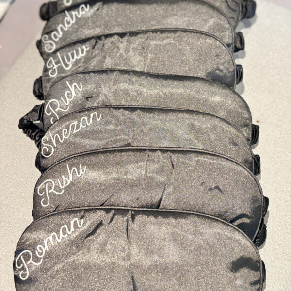 Stack of black sleep masks with names printed on them against a white background.