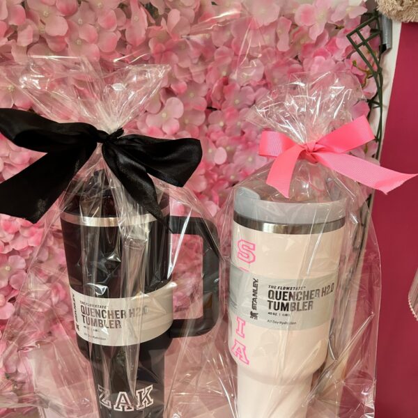 Two stanley-style cups wrapped with ribbons on a pink floral background.