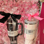 Two stanley-style cups wrapped with ribbons on a pink floral background.