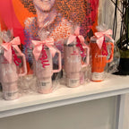 Personalised stanley-style cups with names on a shelf in front of colourful wall art.