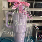 Stanley-style cups with 'Gracie' on it, wrapped in clear plastic with a pink bow, in front of a kitchen counter.