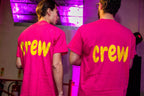 Two people wearing pink 'crew' personalised t-shirts in a dimly lit room with purple lighting.