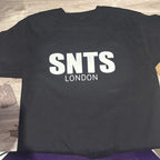 Black t-shirt with 'SNTS LONDON' text on a wooden surface