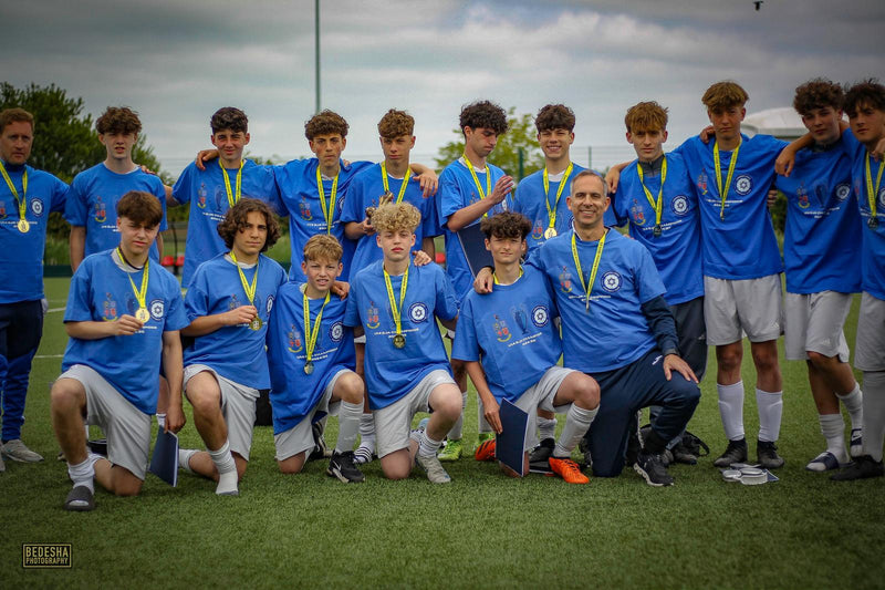 Team of young athletes in blue football tops with medals posing on a grass field.