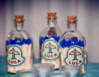 Three glass match stick bottles with cork lids containing matches labelled 'LUCA' on a blurred background.