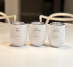 Three white travel cups labelled 'this is TEA', 'this is MATCHA', and 'this is COFFEE' on a light surface.
