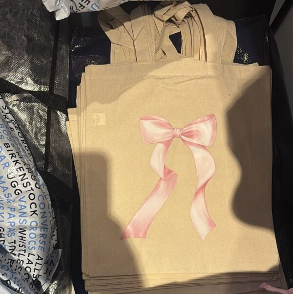 Beige tote bag with a pink bow design on a black surface