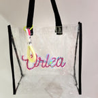 Clear tote bag with colourful text and black straps on a light grey background