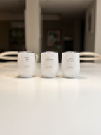Three white travel cups labelled 'this is TEA', 'this is MATCHA', and 'this is COFFEE' on a blurred light surface.