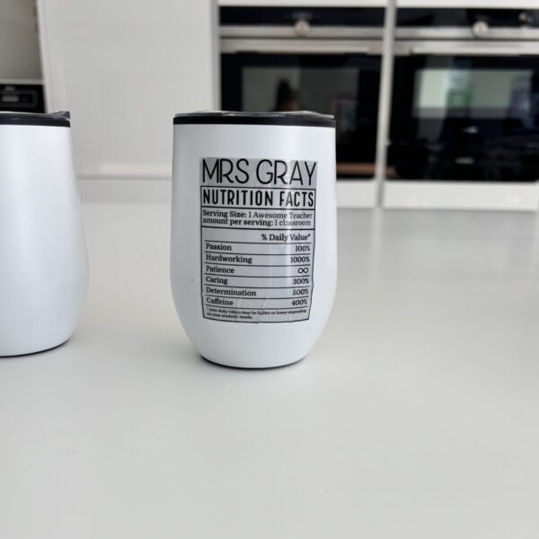 White travel cup with 'Mrs Gray Nutrition Facts' text on a kitchen counter.