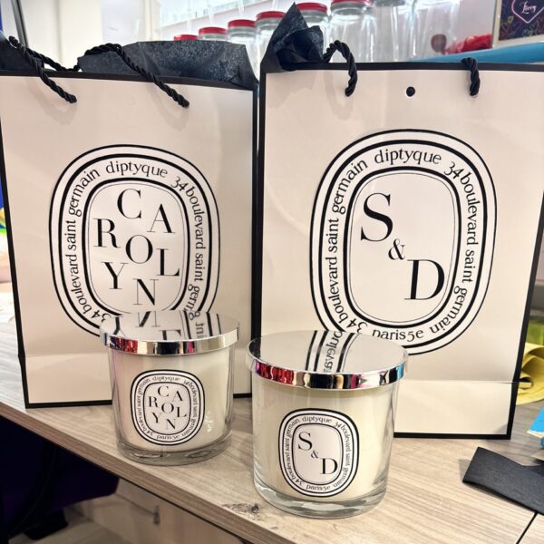 Two Diptyque-style candles with branded packaging on a table.