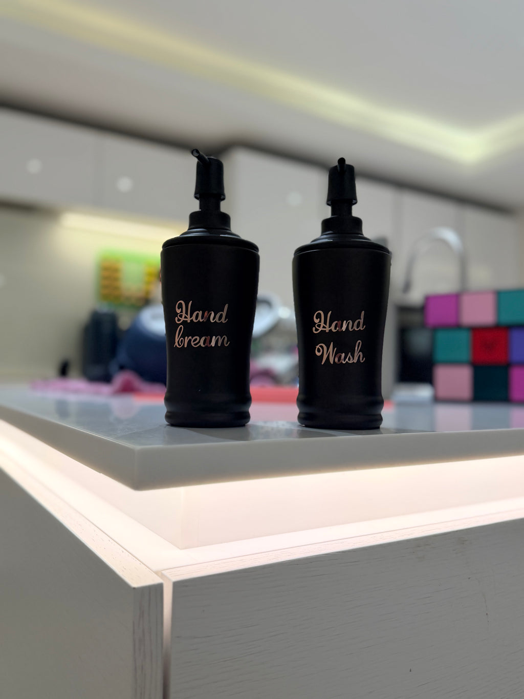 Two black soap bottles labelled 'Hand Cream' and 'Hand Wash' on a counter.