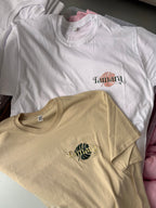Two event t-shirts, one white with a logo and one beige with a different logo, on a surface.