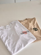 Two folded event t-shirts, one white and one beige, with 'Tamara' branding on a light background.