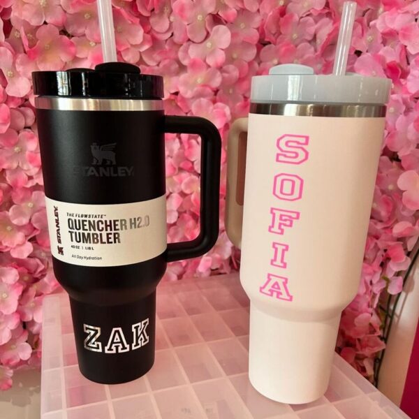 Two stanley-style cups, one black and one pink with 'SOFIA' and 'ZAK' text, against a pink floral background.
