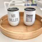 Two white travel cups with personalised text on a wooden tray.