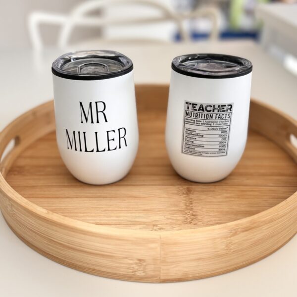 Two white travel cups with personalised text on a wooden tray.