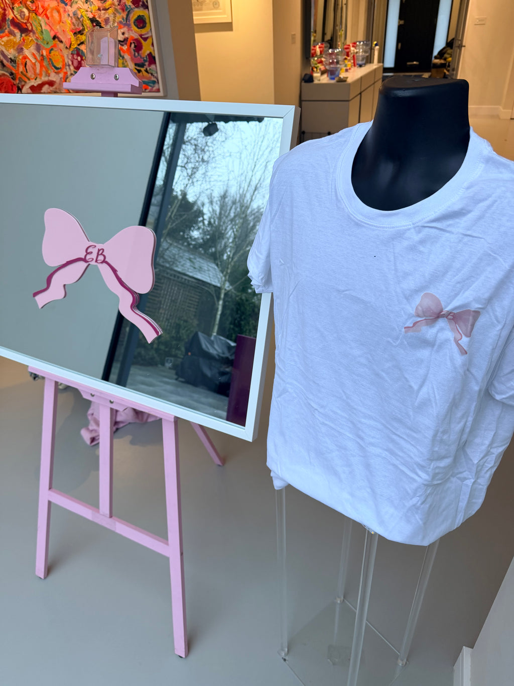 White event t-shirt with pink bow design on a mannequin, displayed next to a mirror reflection.