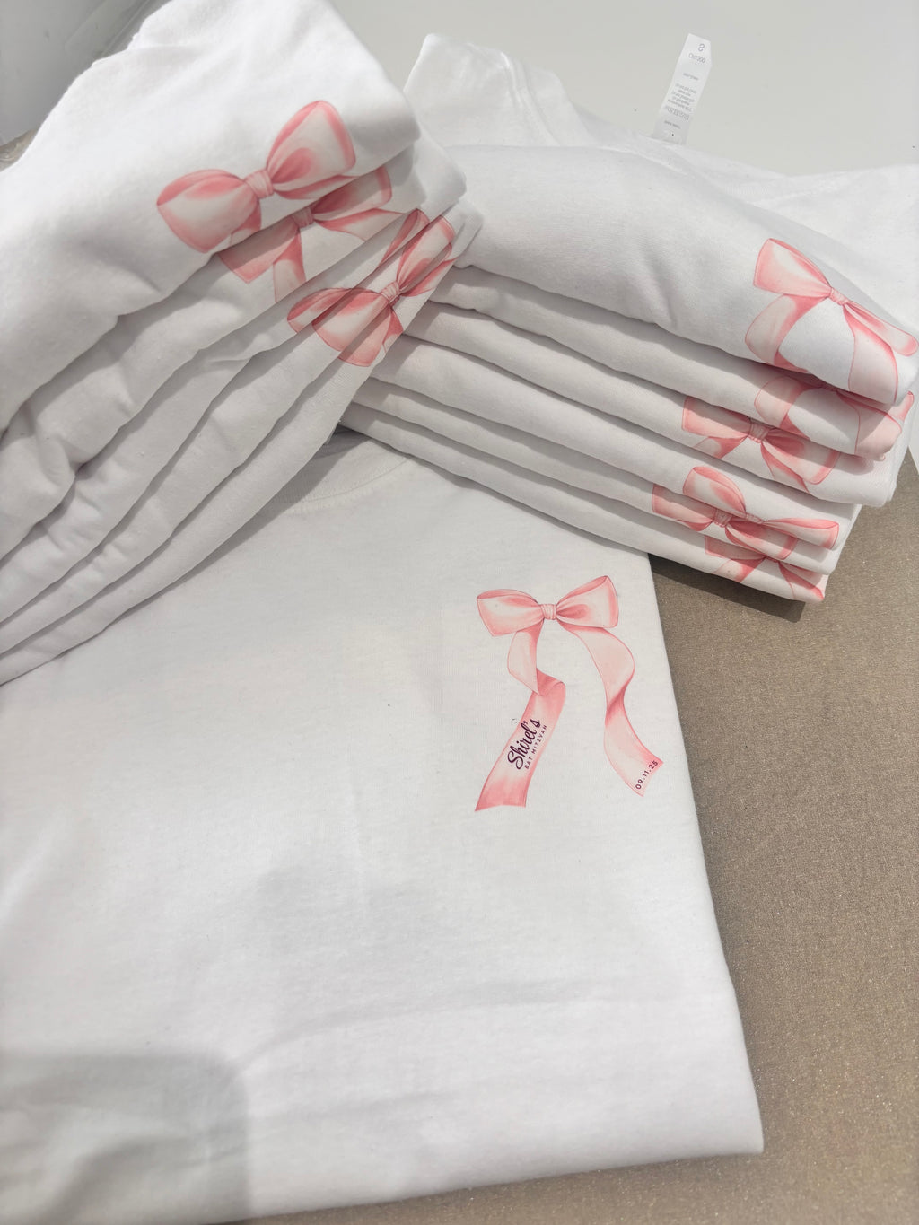 White event t-shirts with pink bows on a neutral background