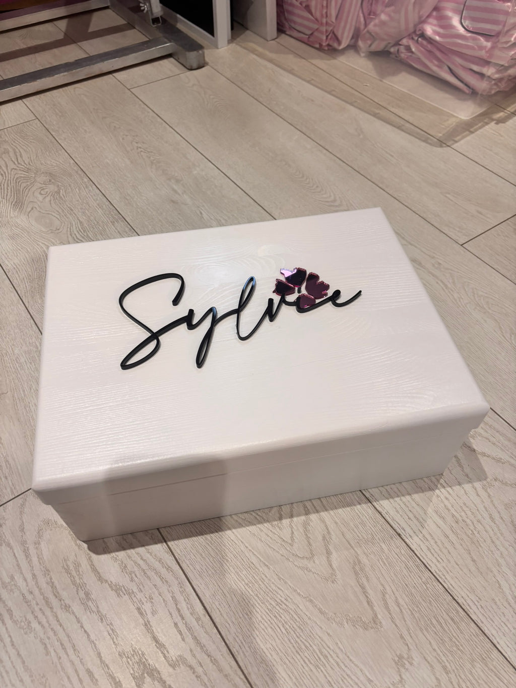 White keepsake box with 'Sylvie' written on it on a wooden floor.