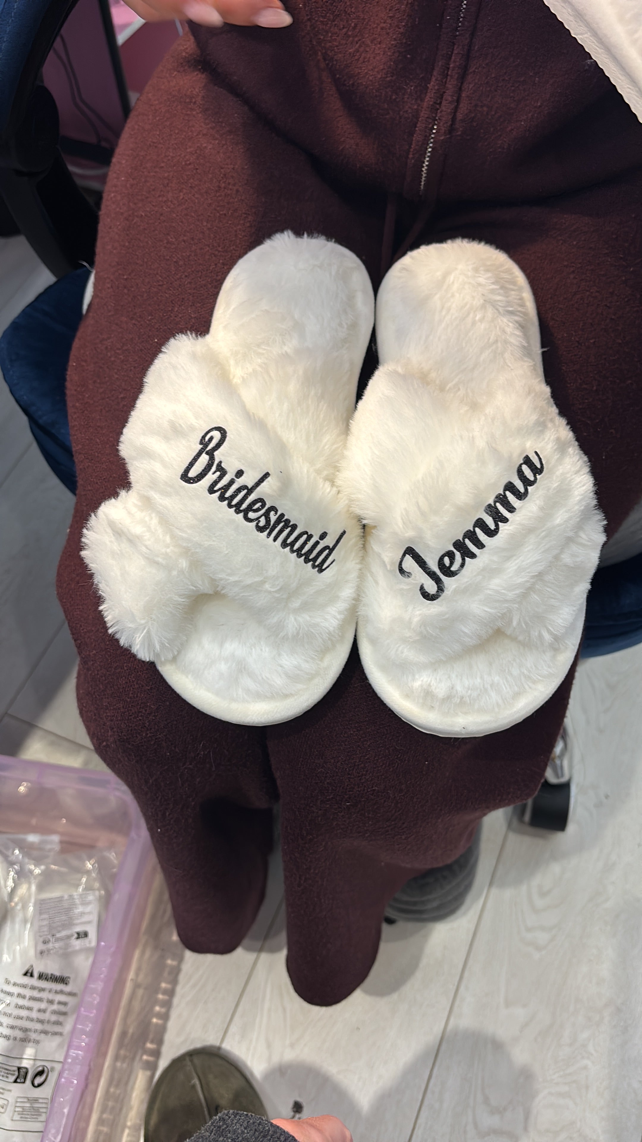 White slippers with 'Jewelry' and 'Bridesmaid' text held by a person in a maroon garment