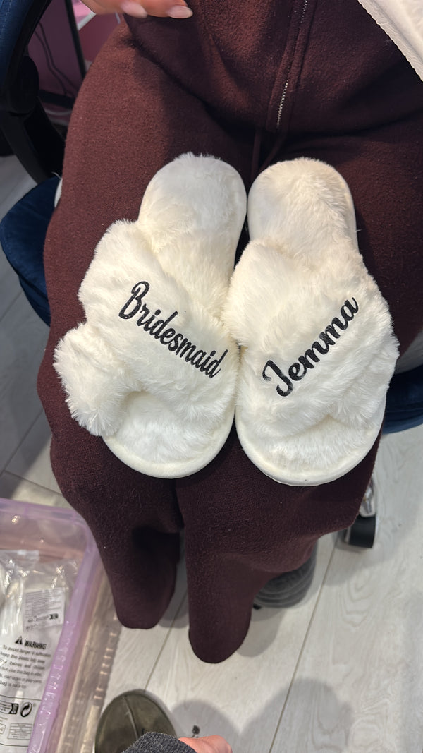 White slippers with 'Jewelry' and 'Bridesmaid' text held by a person in a maroon garment