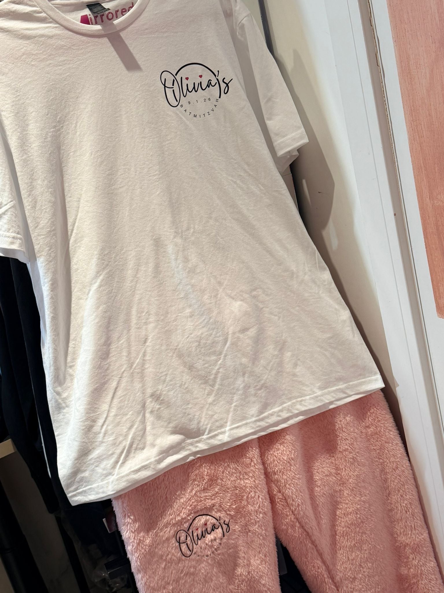 White t-shirt and pink pants with 'Olivia's' logo on a hanger.