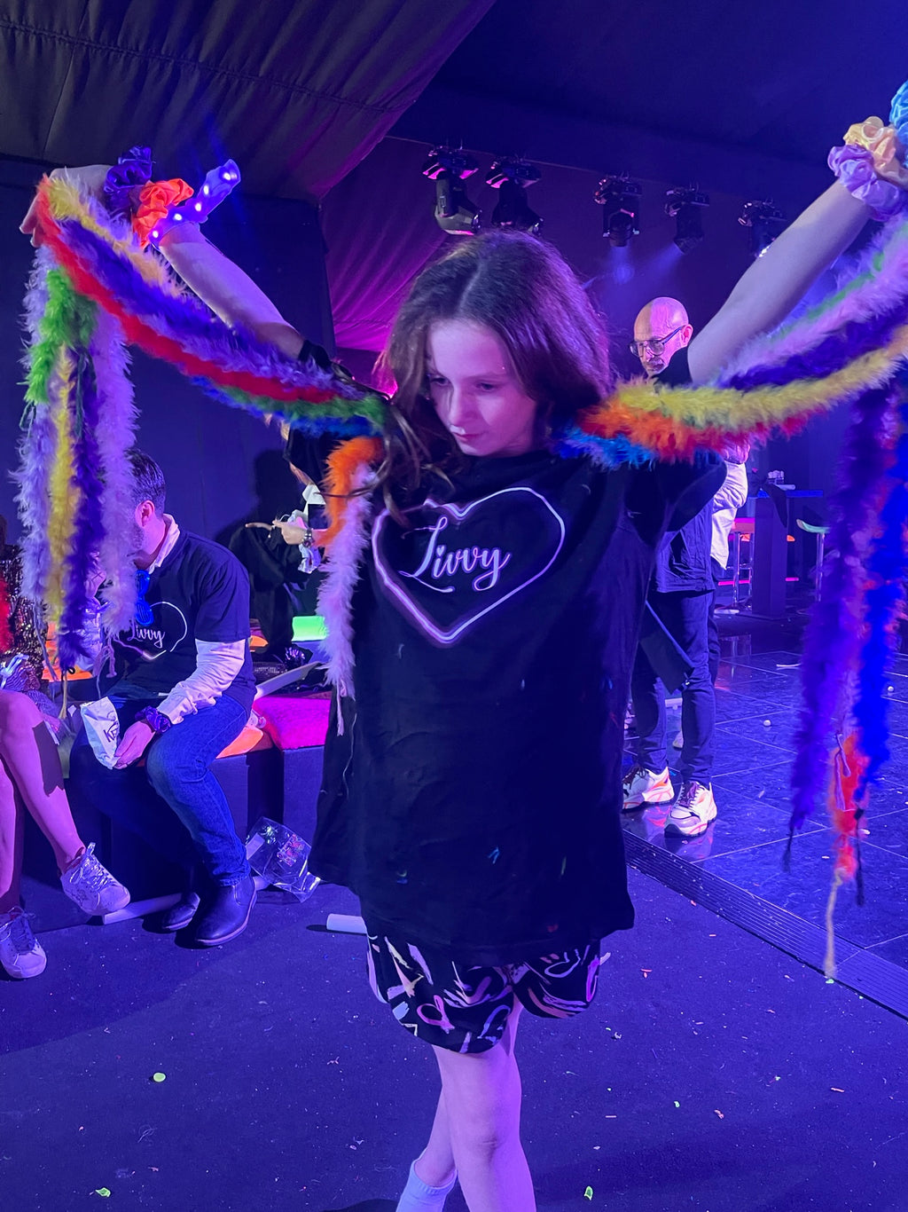 Young girl on a dance floor with colourful decorations and black event t-shirt with customised name 'Livvy'