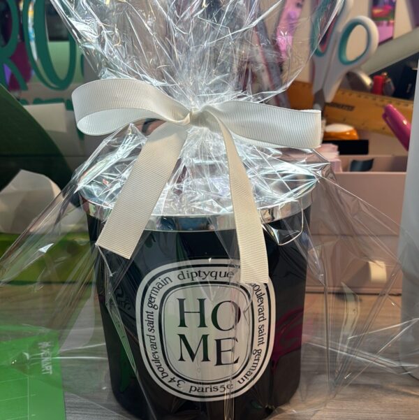 Diptyque-style 'Home' candle wrapped in cellophane with a ribbon on a blurred background