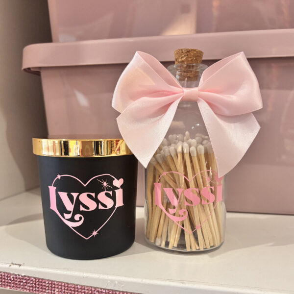 Candle and matchstick jar with 'Lyssi' branding on a pink surface