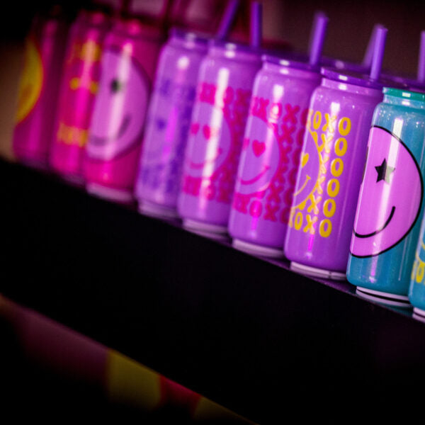 Row of colourful cold cups with straws on a black surface.