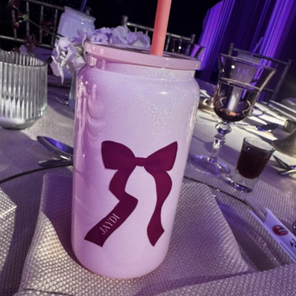 Pink cold cup with a bow design on a table with glasses and a pen.