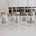 Set of clear cold cups with wooden lids and names printed on them, placed on a white surface.