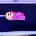Bespoke mirror with 'Hello Summer' design on a stand against a dark wall.