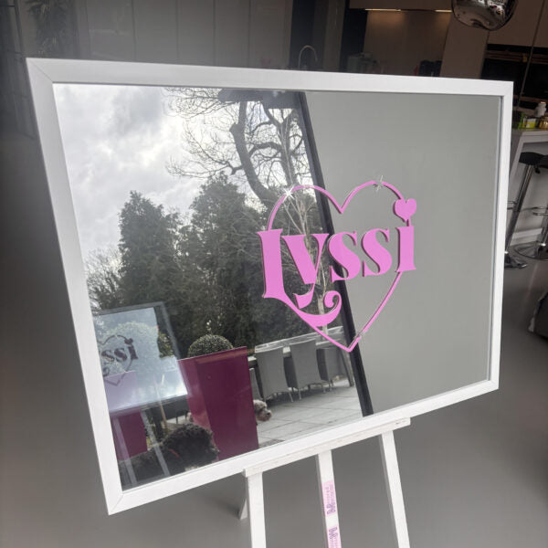 Decorative bespoke mirror with 'Lyssi' in a heart shape on a stand indoors.