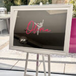 Decorative bespoke mirror with 'Olivia' and a dancer design on a stand outdoors.