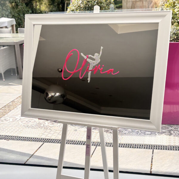 Decorative bespoke mirror with 'Olivia' and a dancer design on a stand outdoors.