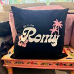 Black logo pillow with 'Romantic' text and palm tree designs on a colourful chair.