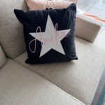 Black logo pillow with a white star and 'Amelie' text on a grey couch.