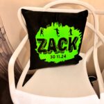 Black logo pillow with green text 'ZACK' on a white chair.
