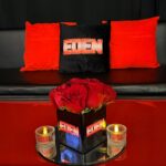 Black logo pillow with red text on a bed next to red roses.