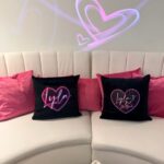 Black logo pillows with pink heart designs amongst pink pillows