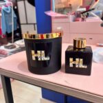 Black personalised candle and diffuser set with gold accents on a blurred store shelf background