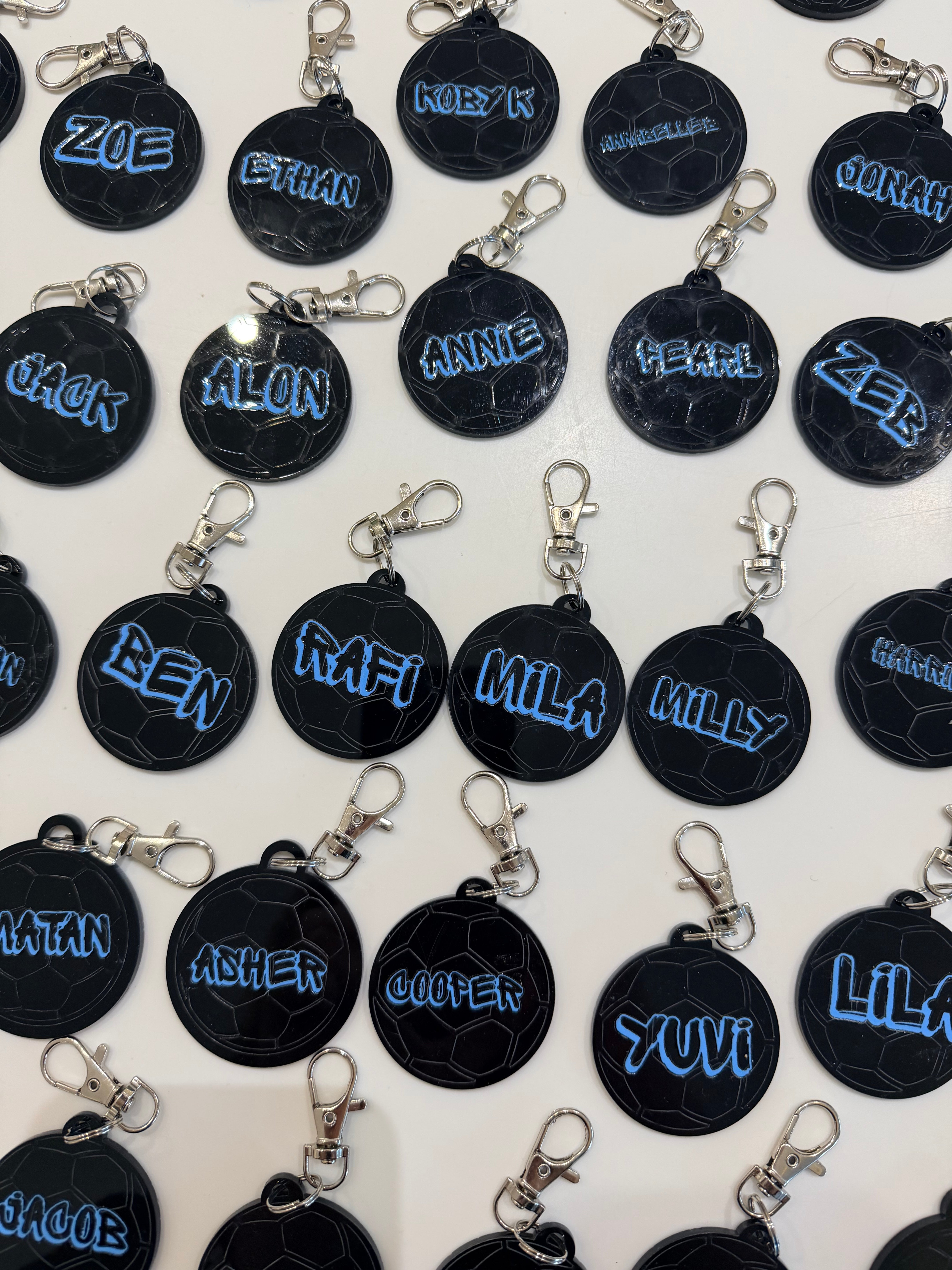Black round keyrings with blue personalised name text on a white background