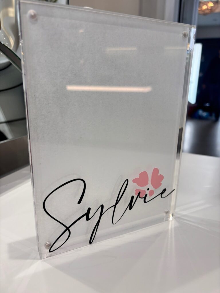 Clear acrylic photo frame with 'Sylvie' and floral design on a white surface