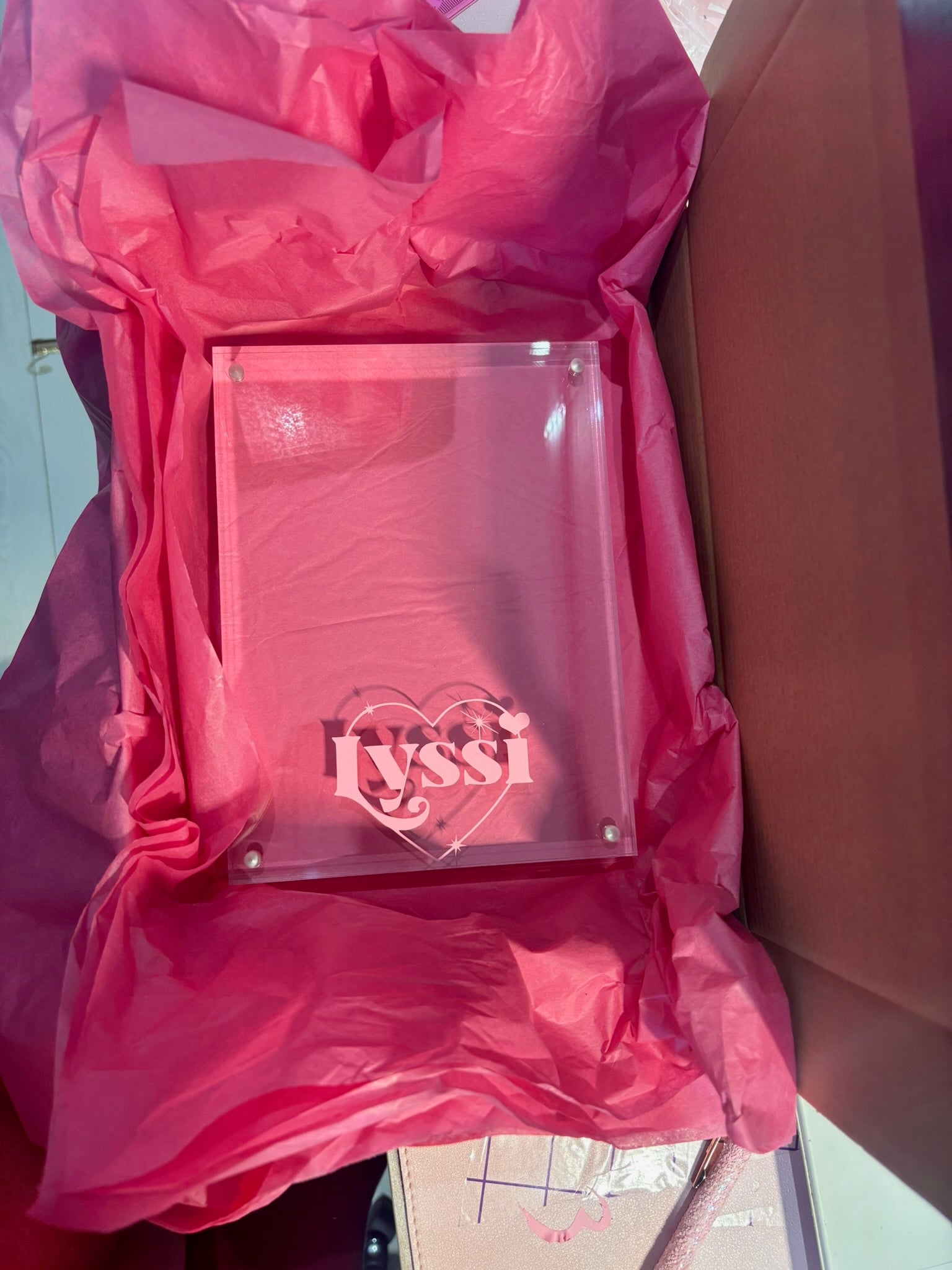 Clear acrylic photo frame with 'lyssi' branding inside a pink protective cover