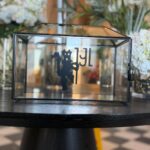 Clear gift card box with a logo on a table with flowers in the background
