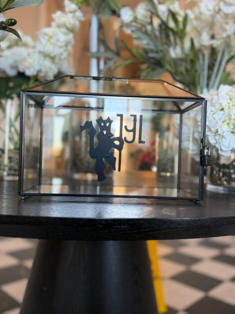 Clear gift card box with a logo on a table with flowers in the background