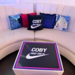 Coby Just Do It box on a white surface with colourful logo pillows in the background